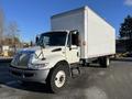 A white 2013 International 4300 box truck with a large cargo area and a flat front design parked at an industrial location