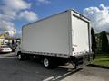 A 2016 Isuzu NPR box truck with a plain white cargo area and a black chassis parked on a concrete surface