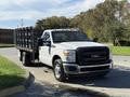 A 2016 Ford F-350 SD pickup truck with a flatbed and tool rack in the back, painted white with black accents and equipped with orange lights on the roof