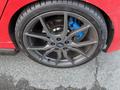 A close-up of a gray alloy wheel with a blue brake caliper mounted on a red 2018 Ford Focus