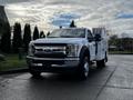 A 2017 Ford F-550 truck with a white utility body and orange lights on the roof parked on a paved surface