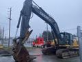 A 2014 John Deere 350G excavator with a large bucket attachment is positioned upright showing its arm and heavy tracks