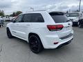 A white 2018 Jeep Grand Cherokee with black wheels and a rear spoiler parked in a lot