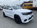 A white 2018 Jeep Grand Cherokee with black rims and a sporty design positioned at an angle showcasing its front and side features