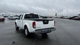 A white 2016 Nissan Frontier pickup truck parked in a spacious lot with a gray sky above