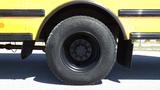 Close-up of a large black tire from a yellow bus showing the tread pattern and wheel hub without any visible damage