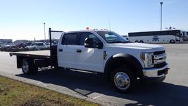 2019 Ford F-550 flatbed truck with a white exterior and metal grill visible in the foreground