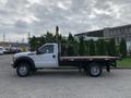 A 2012 Ford F-550 flatbed truck with wooden planks and green shrubs loaded on the flatbed