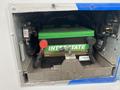 A green Interstate battery secured in a metal compartment with red and black cable connectors