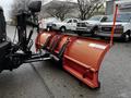 A 2009 Ford F-550 truck equipped with an orange snow plow attachment in the foreground