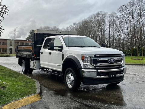 A 2021 Ford F-550 flatbed truck with dual wheels and a white exterior is parked with its bed extended and a tool rack mounted on the back