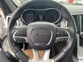 Interior view of a 2018 Jeep Grand Cherokee steering wheel featuring mounted controls and an emblem in the center