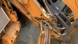 A close-up view of the hydraulic arms and hoses of a 2015 Case 580 backhoe loader showing wear and rust on the metal components