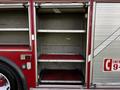 An empty storage compartment of a red 1994 Freightliner FL80 fire truck with metal shelves and red carpet lining