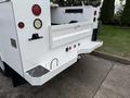 A 2013 Ford F-350 SD with a white utility bed featuring red and amber lights and a textured step with a hook attached to the side