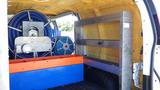 2012 GMC Savana interior featuring a metal shelf unit orange and blue storage containers and a large spool of blue hose