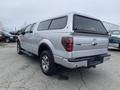 A silver 2014 Ford F-150 with a truck cap on the bed parked at an angle showing the rear and side profiles