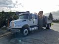 A 2013 International DuraStar 4300 tow truck with an orange crane and a flatbed in a light gray color parked on a street