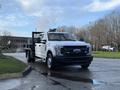 A white 2017 Ford F-350 SD utility truck with a flatbed and an orange warning light on top parked on a street