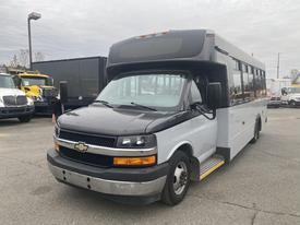 A 2017 Chevrolet Express bus with a black front and white body featuring large windows and a step at the entrance