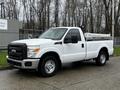 A white 2011 Ford F-250 SD with a black grille and a flatbed attached is parked on a paved surface