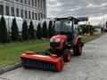 A 2018 Kubota B2650 compact tractor with a front-mounted snow broom attachment in bright orange with a black bristle brush