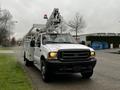 A white 2004 Ford F-450 SD utility truck with a bucket lift mounted on the back and orange lights on top