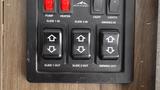 Control panel with buttons for pump, heater, light, slide in/out, and awning out on a wooden surface