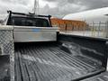 A 2011 Ford F-250 SD truck bed featuring a diamond plate tool box and a textured black liner surface