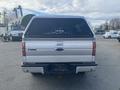 A silver 2014 Ford F-150 truck viewed from the rear with a Leer truck cap on the bed and the Ford logo displayed in the center of the tailgate