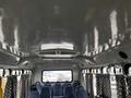 Interior view of a 2012 Chevrolet Express showing rows of blue seats and decorative curtains along the windows with a vent and lights on the ceiling