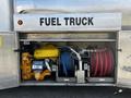 A yellow engine is mounted next to a blue and a red fuel hose inside a storage compartment labeled as a fuel truck