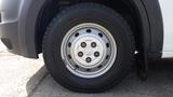 A close-up view of a silver steel wheel with five lug nut holes mounted on a black tire featuring a tread pattern