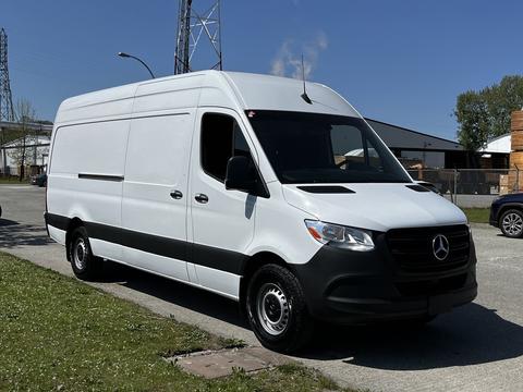 A 2022 Mercedes-Benz Sprinter van in white with a black lower section parked on a street, featuring a streamlined design and large cargo space