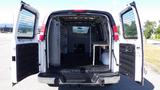 A 2015 GMC Savana van with open rear doors revealing a spacious empty cargo area featuring a partition and a wooden shelf