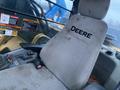 A dirty beige seat inside a John Deere 350G excavator with the word DEERE prominently displayed on the seatback