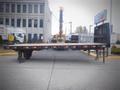 A 2000 flat deck trailer with a wooden surface and metal supports positioned in an industrial area