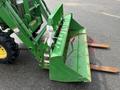 A green John Deere 790 tractor front loader with a bucket and wooden forks attached at the front