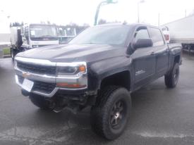 A black 2016 Chevrolet Silverado 1500 with off-road tires and a lifted suspension parked at a commercial location