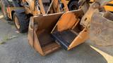 A 2015 Case 580 backhoe loader with a large front bucket and a raised arm showcasing its orange exterior and industrial design