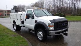 A 2009 Ford F-550 utility truck with a white exterior features a flatbed and tool storage compartments on the side