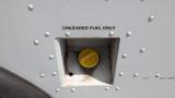 A yellow fuel cap labeled unleaded fuel only attached to the side of a 2011 Ford Econoline vehicle