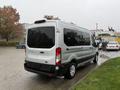 A silver 2019 Ford Transit van with tinted windows and a high roof parked on a wet surface