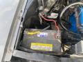 A 1966 Ford Mustang engine compartment showing the car battery with red and yellow cables attached