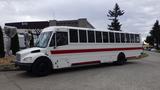 A white 2013 Freightliner M2 106 bus with red stripes parked on a street