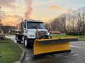 A 2006 Freightliner M2 106 snow plow with a yellow blade positioned in front of the truck ready for clearing snow