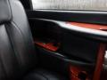 A black leather seat with a wooden armrest featuring a storage compartment and cup holders in a 2008 Cadillac Limousine