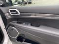 Interior door panel of a 2018 Jeep Grand Cherokee featuring controls for windows and locks with a carbon fiber accent