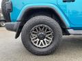 Close-up of a wheel and tire from a blue 2020 Jeep Wrangler showcasing a distinctive alloy rim and rugged off-road tire tread