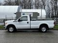 A white 2011 Ford F-250 SD pickup truck with a flatbed and tool rack on the back parked on a pavement